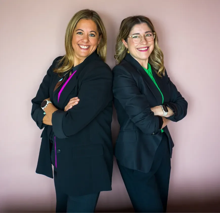 Emily Jaksch and Jessy Warn, owners of HR Gurus, standing back to back in navy suits with their arms folded.
