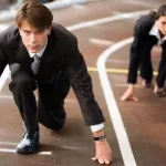 Office workers in suits crouched at the start line of a running track