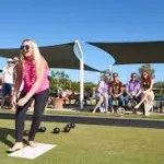 A woman bowling barefoot on a lawn bowls green