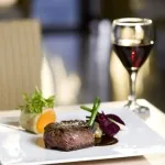 A plated steak dinner with a glass of red wine