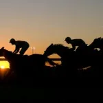 Jockeys on horseback silhouetted against a sunset