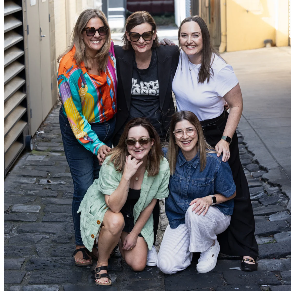 Five members of the HR Gurus team smiling together in a cobbled laneway